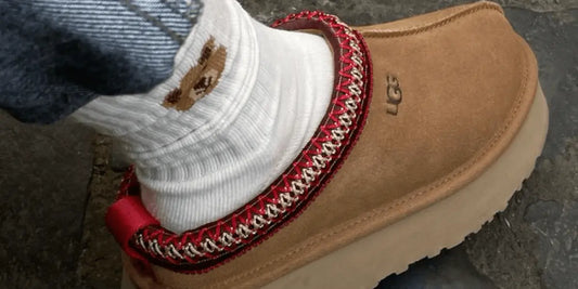 La Ugg Tazz Chestnut portée avec une chaussette ayant une tête d'ourson dessus.