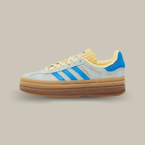 La Adidas Gazelle Bold Almost Blue Yellow vue de côté avec sa base en daim grise, ses trois bandes bleu assprties au heel tab et sa doublure jaune accordée à la languette.