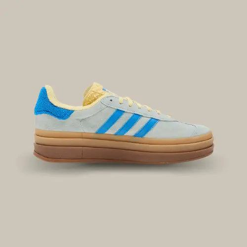 La Adidas Gazelle Bold Almost Blue Yellow vue de côté avec sa base en daim grise, ses trois bandes bleu assprties au heel tab et sa doublure jaune accordée à la languette.