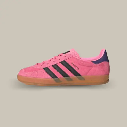 La Adidas Gazelle Indoor Bliss Pink Purple de coté avec sa base en suède rose, ses trois bandes en cuir noir, son talon en cuir violet et sa semelle en gomme de caoutchouc.