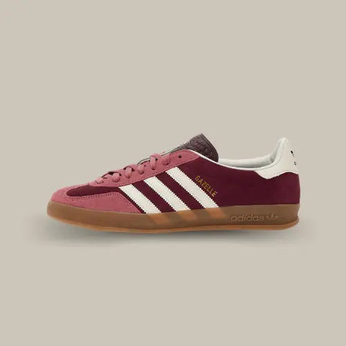 La Adidas Gazelle Indoor Maroon Preloved Crimson vue de côté avec sa base de couleur bordeaux avec des superpositions en dail rose. On retrouve les trois bandes blanches accordés au heel tab.