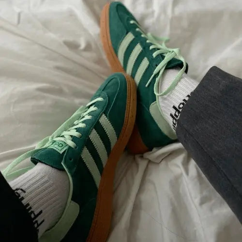 La Adidas Handball Spezial Collegiate Green Semi Green Spark porté avec un pantalon gris foncé.