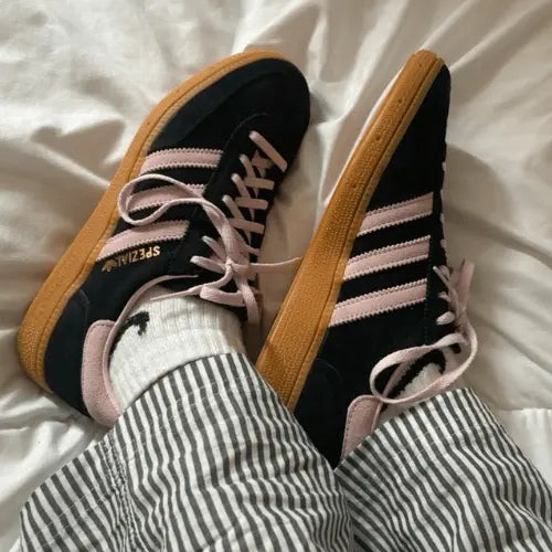 La Adidas Handball Spezial Core Black Clear Pink Gum porté avec un pantalon rayé.