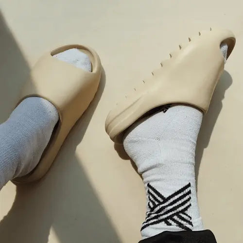 La Adidas Yeezy Slide Bone Restock Pair portée avec des chaussettes blanches.