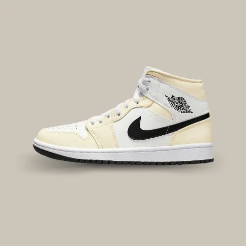 La Air Jordan 1 Mid Coconut Milk vue de côté avec son cuir allant du blanc au blanc cassé et son swoosh noir accordé à la semelle extérieure.