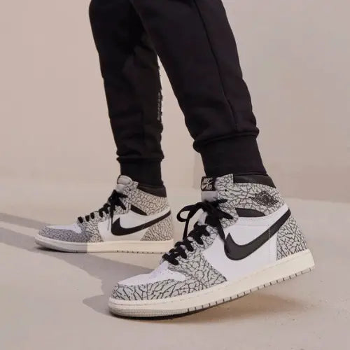 La Air Jordan 1 Retro High OG White Cement portée avec un pantalon noir.