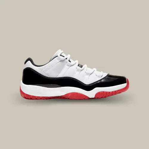 La Air Jordan 11 Low White Bred vue de côté avec sa base en mesh blanc, son mudguard en cuir noir verni, sa midsole blanche et son outsole rouge.