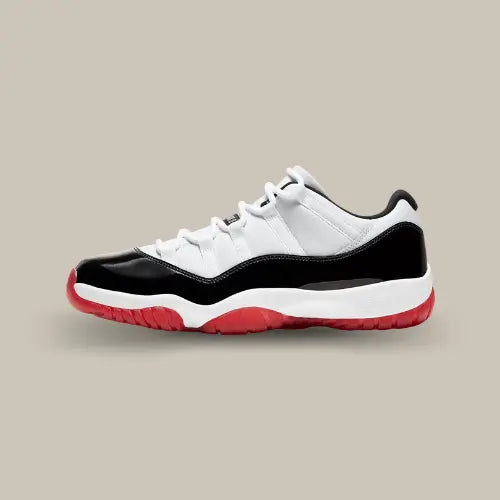 La Air Jordan 11 Low White Bred vue de côté avec sa base en mesh blanc, son mudguard en cuir noir verni, sa midsole blanche et son outsole rouge.