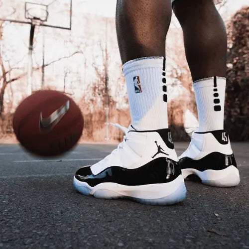 La Air Jordan 11 Retro Concord (2018) portée par un basketteur sur un playground avec un ballon de basket Nike.