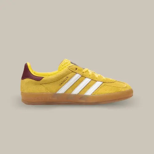 La Adidas Gazelle Indoor Bright Yellow Burgundy de coté avec sa base en daim jaune, ses trois bandes blanches, son talon en cuir et sa semelle en gomme.