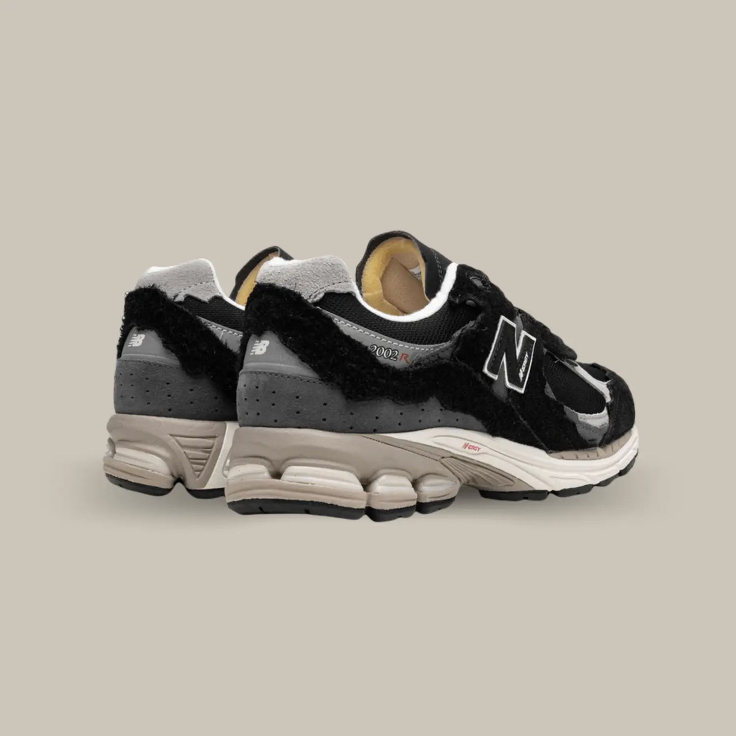 La New Balance 2002R Protection Pack Black de dos avec une base en mesh noir accompagnée de superpositions en daim ton-sur-ton au look déchiré pour donner le fidèle aspect déconstruit.