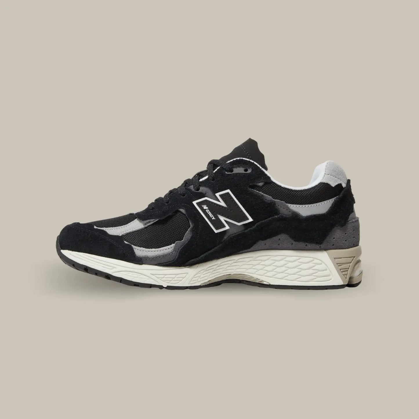 La New Balance 2002R Protection Pack Black de coté avec une base en mesh noir accompagnée de superpositions en daim ton-sur-ton au look déchiré pour donner le fidèle aspect déconstruit.