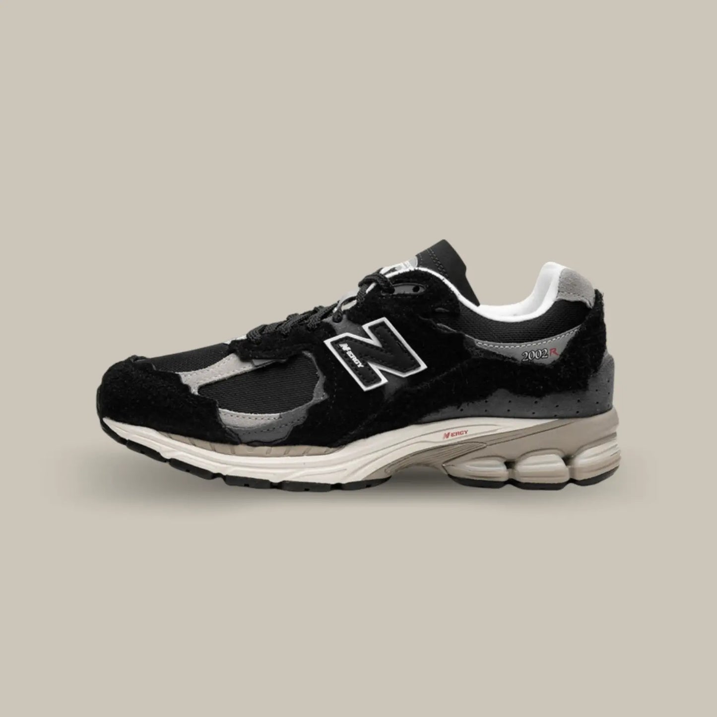 La New Balance 2002R Protection Pack Black de coté avec une base en mesh noir accompagnée de superpositions en daim ton-sur-ton au look déchiré pour donner le fidèle aspect déconstruit.