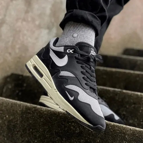 La Nike Air Max 1 Patta Black Grey portée avec pantalon noir et des chaussettes grises.