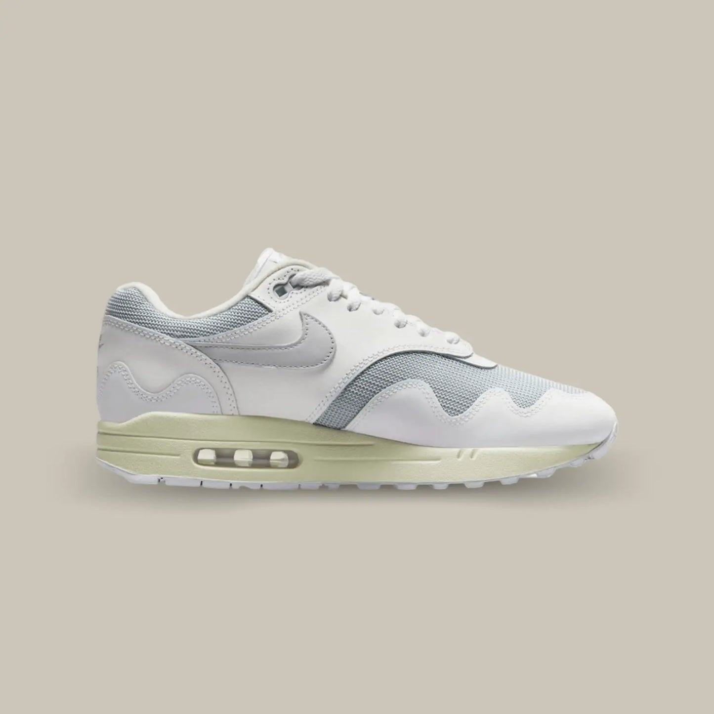 La Nike Air Max 1 Patta White Grey de coté avec une base en mesh gris complétée par des superpositions de cuir blanc.